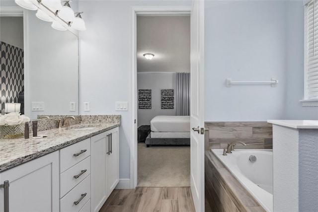 bathroom with tiled tub, vanity, and wood-type flooring