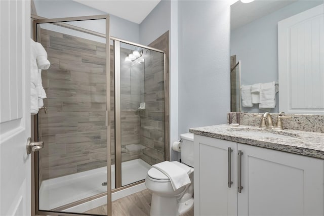 bathroom with vanity, hardwood / wood-style floors, a shower with door, and toilet