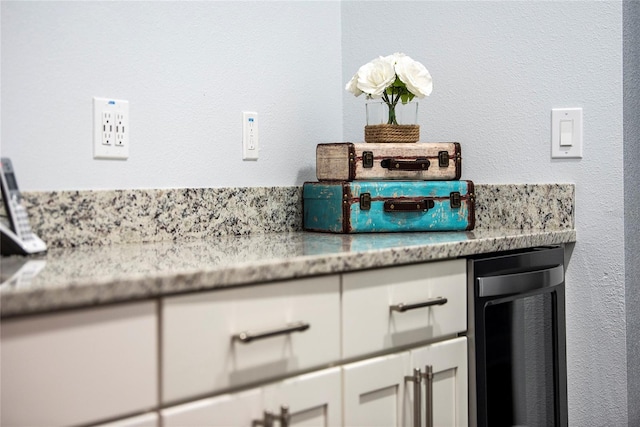 room details with white cabinetry, light stone counters, and wine cooler