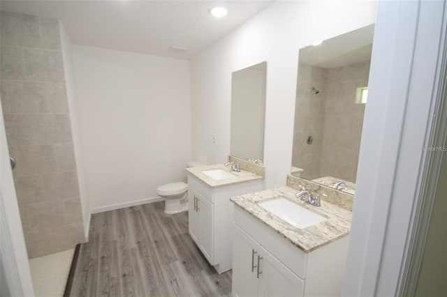 bathroom featuring hardwood / wood-style flooring, vanity, toilet, and a tile shower