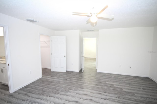 unfurnished bedroom with ceiling fan, hardwood / wood-style floors, ensuite bathroom, a spacious closet, and a closet