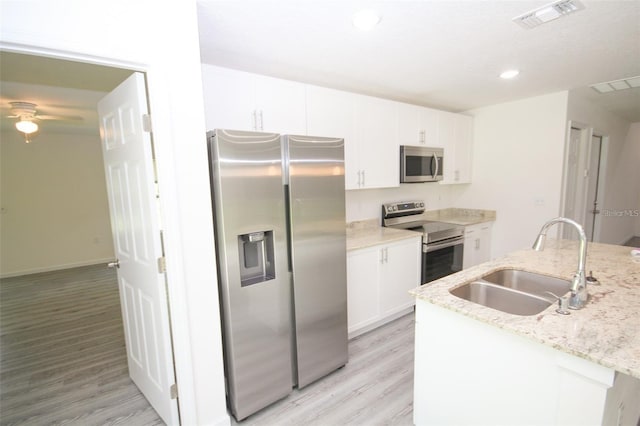 kitchen with sink, light wood-type flooring, appliances with stainless steel finishes, light stone countertops, and white cabinets