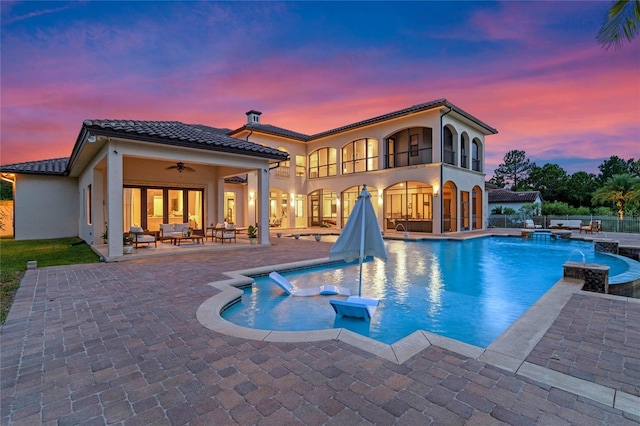 pool at dusk with outdoor lounge area, an in ground hot tub, pool water feature, ceiling fan, and a patio area