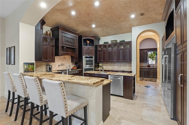 kitchen with appliances with stainless steel finishes, light stone counters, a kitchen bar, decorative backsplash, and kitchen peninsula