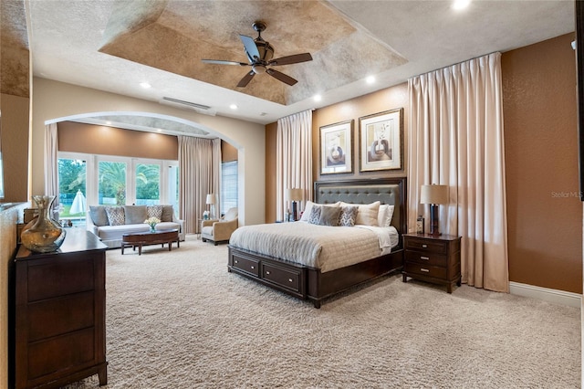 carpeted bedroom with ceiling fan, a tray ceiling, and a textured ceiling