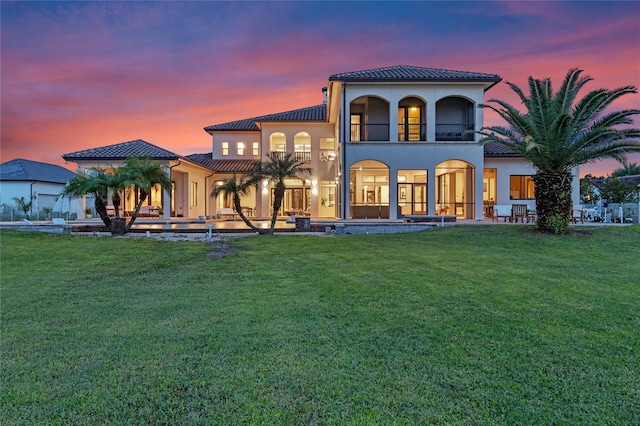 back house at dusk featuring a lawn and a balcony