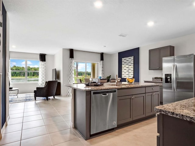 kitchen with sink, stainless steel appliances, light stone countertops, and a center island with sink