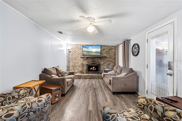 living room featuring hardwood / wood-style flooring, ceiling fan, ornamental molding, a textured ceiling, and a brick fireplace