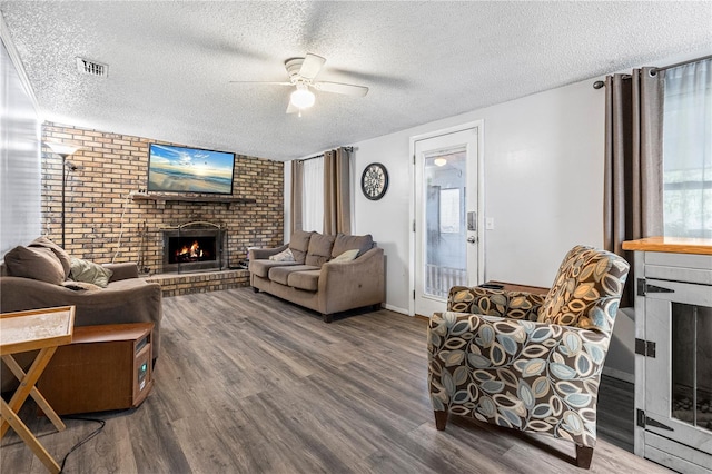 living room featuring wood-type flooring, ceiling fan, a textured ceiling, and a fireplace