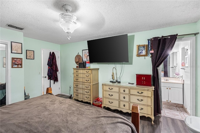 bedroom featuring ensuite bath, ceiling fan, hardwood / wood-style floors, a textured ceiling, and a closet