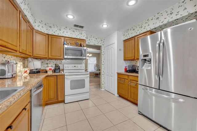 kitchen with wallpapered walls, light tile patterned floors, visible vents, brown cabinets, and stainless steel appliances