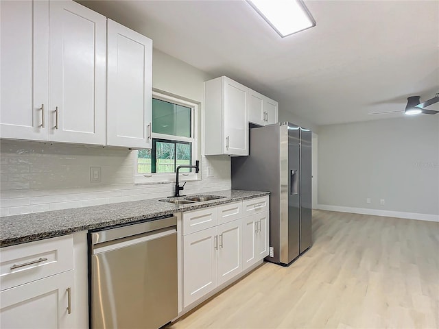 kitchen with stainless steel appliances, white cabinetry, sink, and dark stone counters