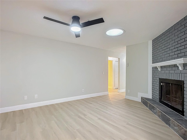 unfurnished living room featuring a brick fireplace, light hardwood / wood-style flooring, and ceiling fan