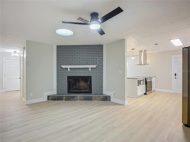 unfurnished living room featuring ceiling fan, a fireplace, light hardwood / wood-style floors, and a textured ceiling