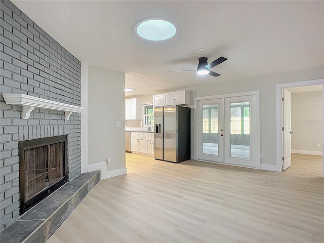 unfurnished living room with sink, ceiling fan, light hardwood / wood-style floors, a brick fireplace, and french doors