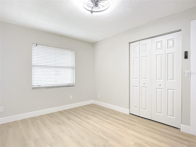 unfurnished bedroom with a textured ceiling, light wood-type flooring, and a closet