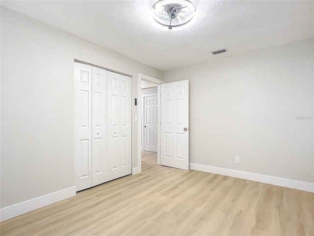 unfurnished bedroom with a textured ceiling, a closet, and light wood-type flooring