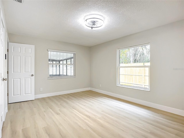 spare room featuring a healthy amount of sunlight, a textured ceiling, and light wood-type flooring