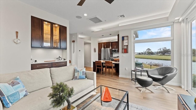 living room with ceiling fan, a water view, and light wood-type flooring