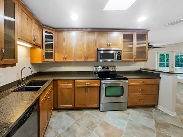 kitchen with sink, a skylight, dark stone countertops, ceiling fan, and stainless steel appliances