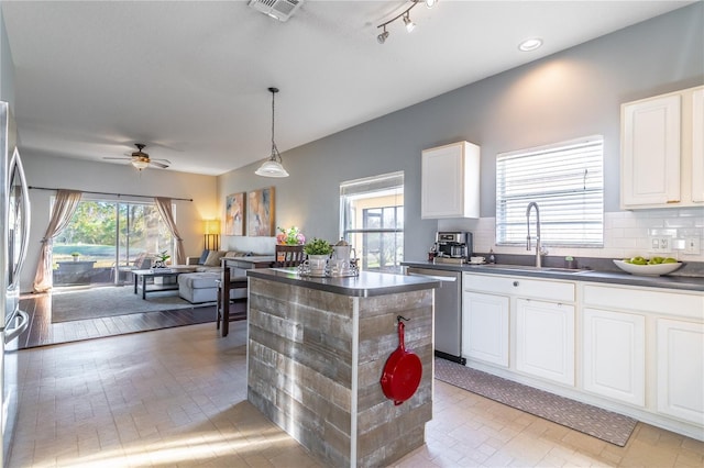 kitchen featuring sink, stainless steel dishwasher, a kitchen island, pendant lighting, and white cabinets