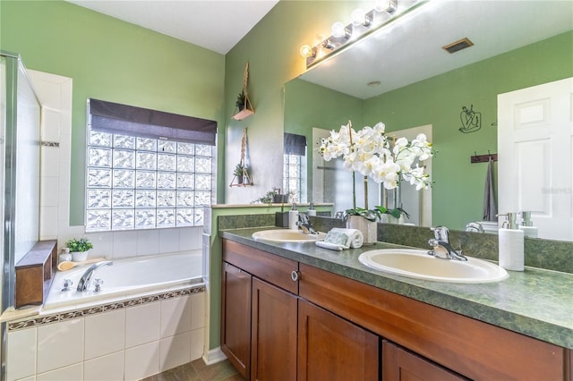 bathroom with tiled tub, vanity, and a healthy amount of sunlight