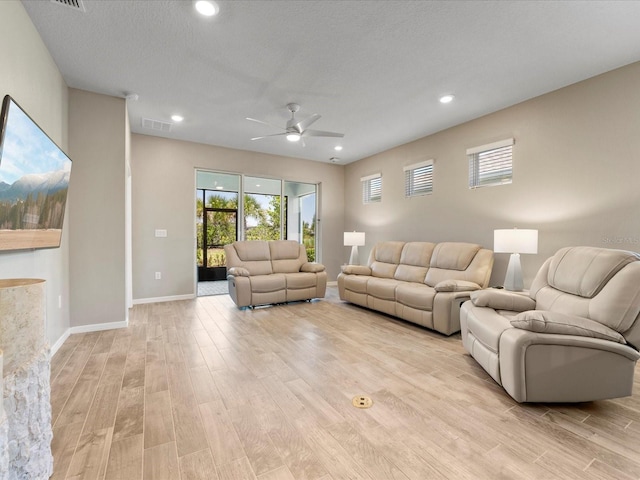 living room featuring ceiling fan, a textured ceiling, and light wood-type flooring