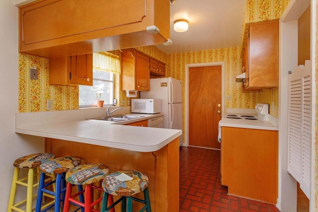 kitchen with white appliances, a kitchen breakfast bar, kitchen peninsula, and sink