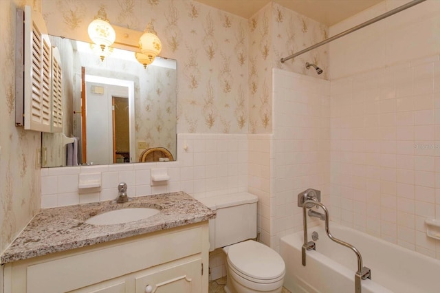 full bathroom with tiled shower / bath, tile walls, vanity, and toilet