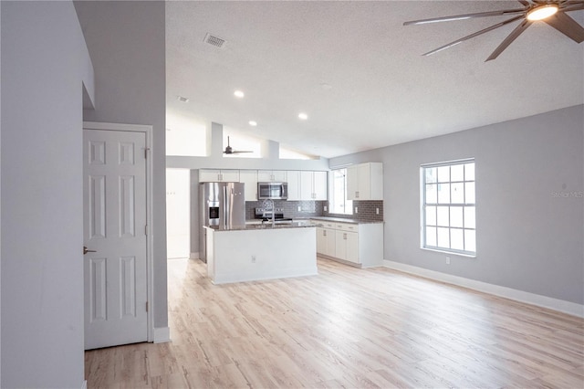 kitchen featuring vaulted ceiling, white cabinets, backsplash, a center island, and stainless steel appliances