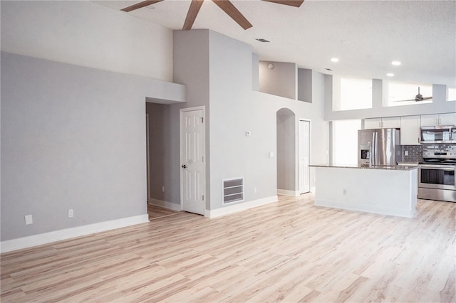 kitchen with ceiling fan, backsplash, a towering ceiling, stainless steel appliances, and white cabinets