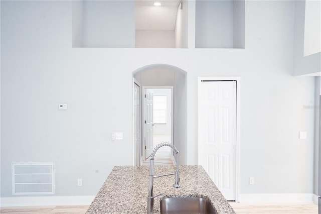 kitchen with a high ceiling, light stone countertops, sink, and light wood-type flooring