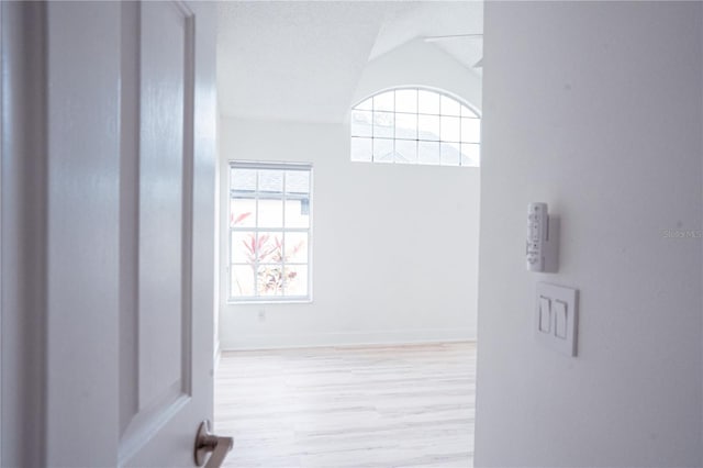 hall featuring vaulted ceiling, a textured ceiling, and light hardwood / wood-style flooring