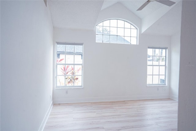 empty room with high vaulted ceiling, a wealth of natural light, ceiling fan, and light hardwood / wood-style flooring