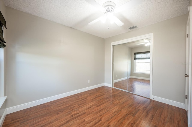 unfurnished bedroom featuring dark wood-type flooring, ceiling fan, a closet, and a textured ceiling