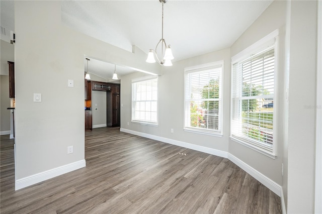 unfurnished dining area featuring lofted ceiling, hardwood / wood-style floors, and an inviting chandelier