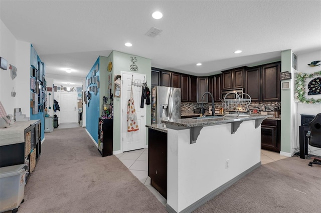 kitchen with a breakfast bar area, appliances with stainless steel finishes, backsplash, an island with sink, and light tile patterned flooring