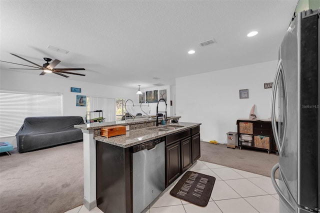 kitchen with appliances with stainless steel finishes, sink, light colored carpet, dark brown cabinetry, and light stone countertops