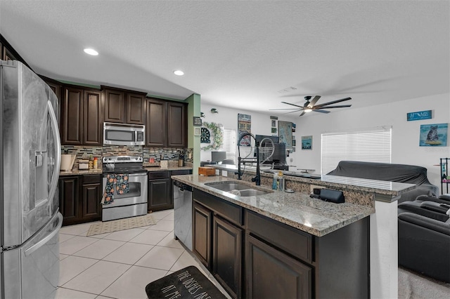 kitchen with light tile patterned flooring, a kitchen island with sink, dark brown cabinetry, stainless steel appliances, and a textured ceiling