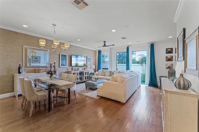 living room with an inviting chandelier, light hardwood / wood-style flooring, ornamental molding, and a textured ceiling