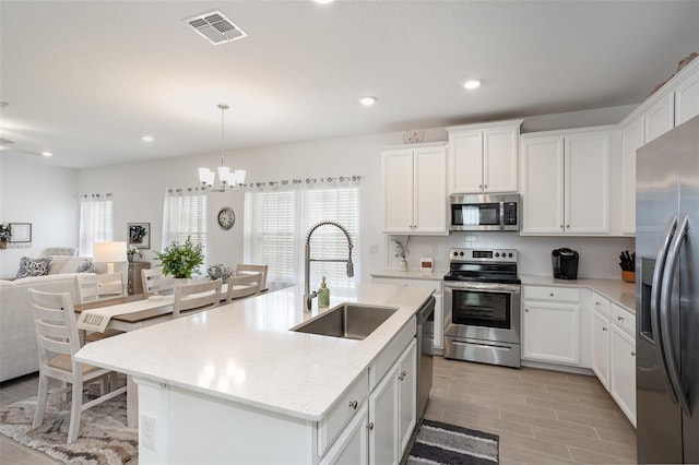 kitchen with sink, a kitchen island with sink, white cabinetry, stainless steel appliances, and light stone counters