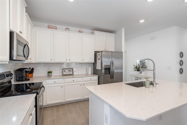 kitchen with sink, appliances with stainless steel finishes, light stone countertops, an island with sink, and white cabinets