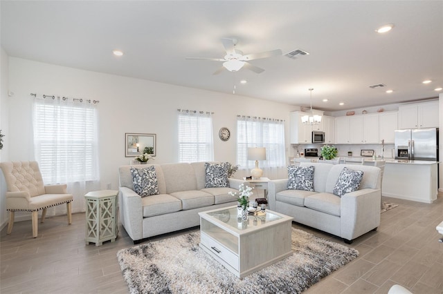 living room featuring ceiling fan with notable chandelier and light hardwood / wood-style floors