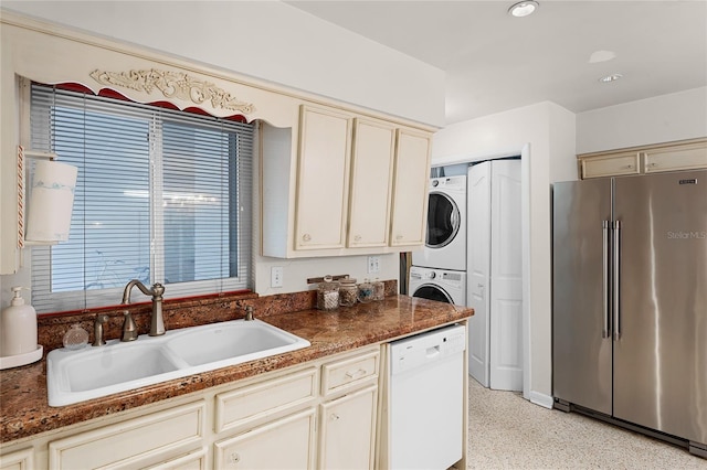 kitchen featuring stacked washer and dryer, sink, high end refrigerator, white dishwasher, and cream cabinetry