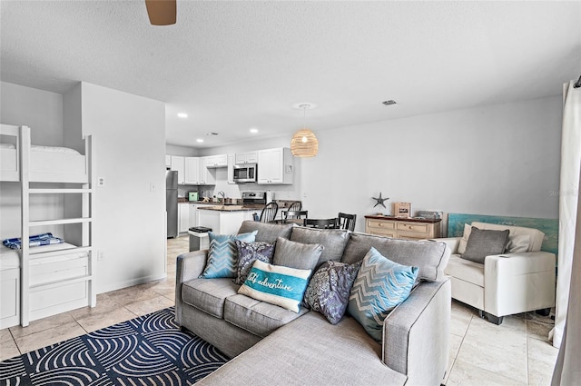 living room with ceiling fan, sink, a textured ceiling, and light tile patterned floors