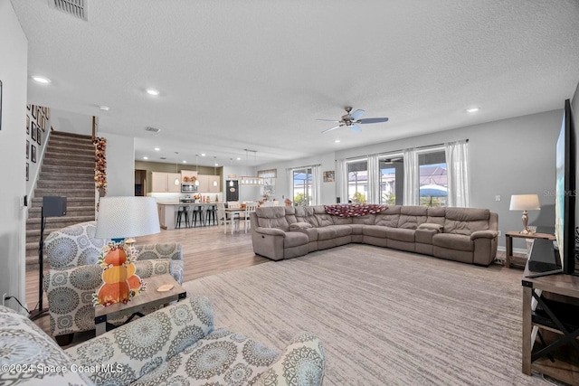 living room with ceiling fan, light hardwood / wood-style flooring, and a textured ceiling