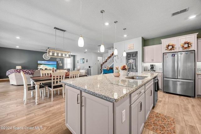 kitchen featuring sink, stainless steel refrigerator, a textured ceiling, a center island with sink, and decorative light fixtures