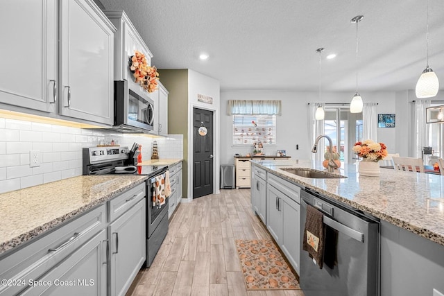 kitchen with sink, backsplash, stainless steel appliances, light hardwood / wood-style floors, and decorative light fixtures