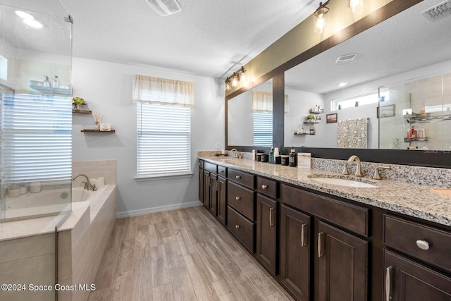 bathroom featuring tiled tub, vanity, wood-type flooring, and a textured ceiling