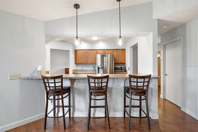 kitchen featuring a breakfast bar, appliances with stainless steel finishes, light stone counters, decorative light fixtures, and kitchen peninsula